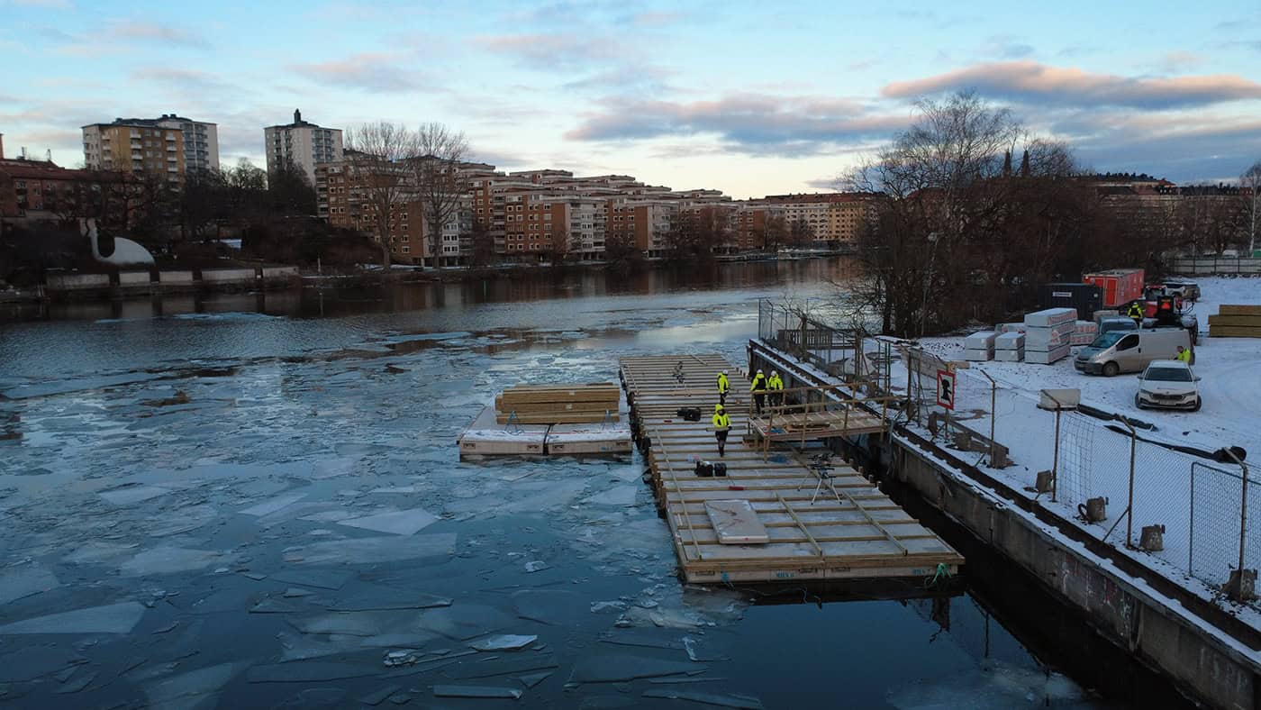 Eisboje und Hafenanlage am Fluss im Winter mit Stadt im Hintergrund.